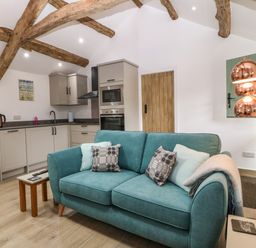 A kitchen and sitting area with exposed wooden beams a teal sofa and modern kitchen units at Y Stabl in Dyffryn Ardudwy