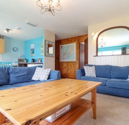 A living room with blue sofas and a wooden coffee table with kitchen area in the background at Skylarks Trevellas Nr St Agnes