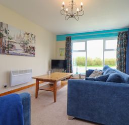 A living room with blue sofas a wooden coffee table a television and large windows with curtains at Skylarks Trevellas Nr St Agnes