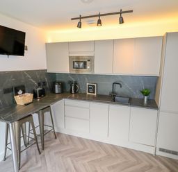 A kitchen with grey cabinets a black countertop a mounted TV and two metal stools at Valley Lodge 4 - North Wales Eco Lodges in Graigfechan near Ruthin