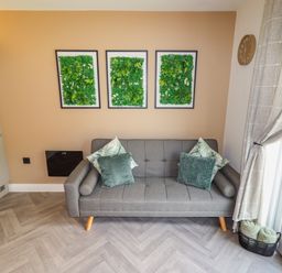 A gray sofa with four cushions below three framed green leaf wall decorations in a living room at Valley Lodge 4 - North Wales Eco Lodges Graigfechan near Ruthin