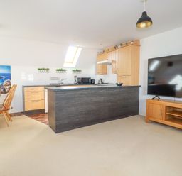 A kitchen and dining area with wooden cabinets a dining table and chairs and a large flat screen tv at 20 Keay Heights in St Austell