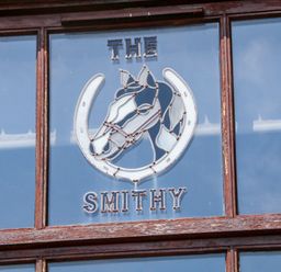 A stained glass window with a horse head and horseshoe design and the words the smithy at The Old Smithy in Lynton