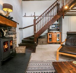 A living room with a wood burning stove wooden stairs and a black chair at The Old Smithy in Lynton