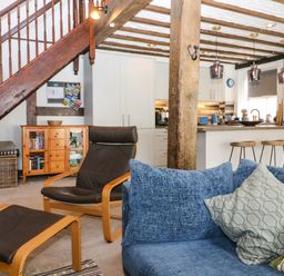 An open living space with a blue sofa and pillows a brown chair and footrest a wooden cabinet and a kitchen area with stools and pendant lights at The Old Smithy in Lynton