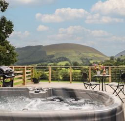 An outdoor area with a hot tub and dining table at Caban Tirion Dinas Mawddwy near Dolgellau