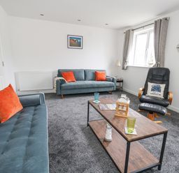 A living room with two blue sofas with orange pillows a black armchair a wooden coffee table with glasses and decor at Dotties Retreat in Weymouth