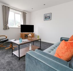 A living room with a blue sofa with orange pillows a wooden coffee table a black reclining chair and a television at Dotties Retreat in Weymouth