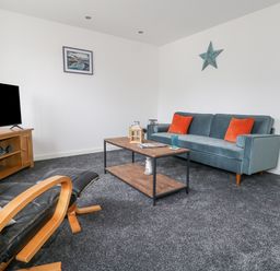 A living room with a blue sofa with orange cushions a wooden coffee table a black leather chair and a wooden TV stand at Dotties Retreat in Weymouth