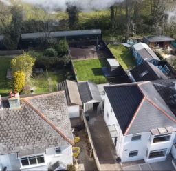 An aerial view of backyards with green lawns and garden structures behind houses at The Swanage Rail Lookout in Swanage
