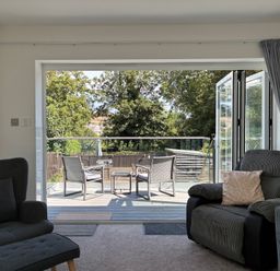 A living room with armchair and sofa leading to a patio at The Swanage Rail Lookout in Swanage