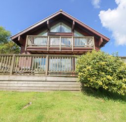 A wooden house with two balconies and a shrub in front at The Willows in Winnard's Perch near St Columb Major