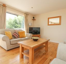 A living room with a sofa, armchairs, wooden coffee table, television, and mirror at The Willows in Winnard's Perch near St Columb Major