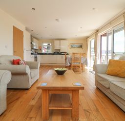 A living room with sofas and a wooden coffee table next to a kitchen and dining area at The Willows Winnard's Perch near St Columb Major