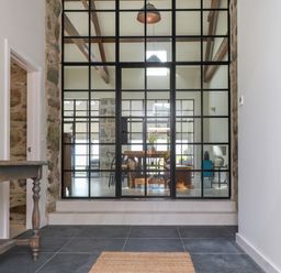 A hallway with a wooden table and tiled floor facing a glass partition with metal frames at Beudy Mawr in Cwmystradllyn near Tremadog