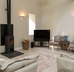 A living room with a wood stove a basket of firewood a television two armchairs a side table with a lamp and a sofa at Beudy Mawr in Cwmystradllyn near Tremadog