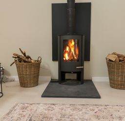 A wood stove with a fire burning two baskets of firewood on either side and a patterned rug in front at Beudy Mawr in Cwmystradllyn near Tremadog