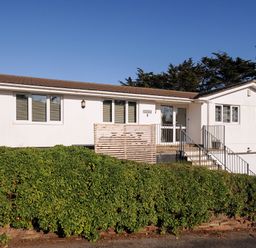 A white single-story house with multiple windows and a staircase leading to the front door at Surf Break in Polzeath