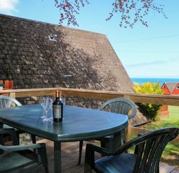 A balcony with a plastic table and chairs with a bottle and glasses overlooking rooftops and the sea at Chalet 58 - The Beach House in Kingsdown