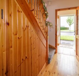 A hallway with wooden staircase and open door leading outside at 46 Dunalinn in Culdaff County Donegal