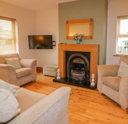 A living room with beige armchairs a fireplace and a wall-mounted television at 46 Dunalinn in Culdaff County Donegal