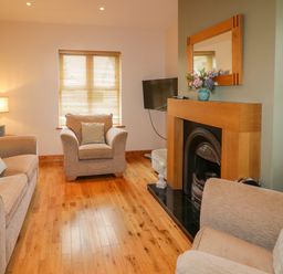 A living room with beige sofas a wooden floor a window with blinds and a fireplace at 46 Dunalinn in Culdaff County Donegal