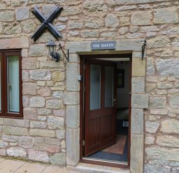An open wooden door and window on a stone wall with a sign above the door saying The Haven in Norham