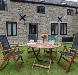 A wooden outdoor table with four chairs on grass in front of a stone building at The Haven in Norham