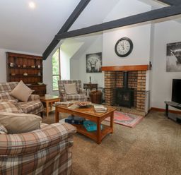A living room with plaid armchairs a wooden coffee table a brick fireplace and a television at The Haven in Norham