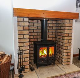 A burning wood stove with a brick surround and wooden beam mantel at The Haven in Norham