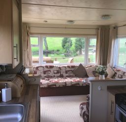 A kitchen and living room with a sink stove sofa cushions and window overlooking a grassy area at Hollie in Raglan