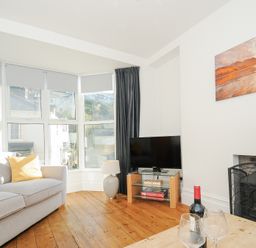 A living room with a sofa a television on a glass stand a lamp and a coffee table with wine glasses at Albert House in Looe