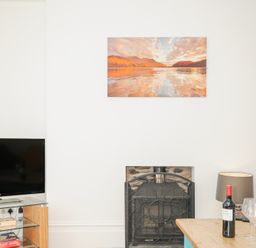 A wall with a mounted landscape painting above a fireplace next to a tv on a glass stand and a table with a wine bottle and glasses at Albert House in Looe