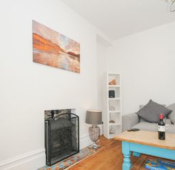 A living room with a fireplace a grey sofa a wooden coffee table with a blue base and a white shelf at Albert House in Looe