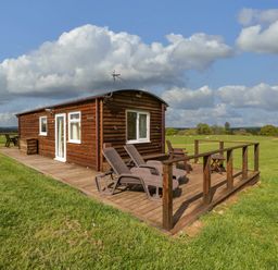 A wooden cabin with deck chairs and a table on a grassy field at Poppy in Raglan