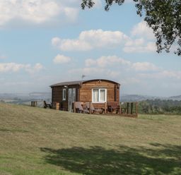 A wooden cabin with a deck and chairs at Poppy in Raglan