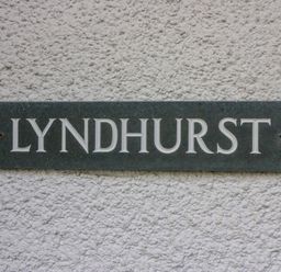 A dark rectangular plaque with the word Lyndhurst on a textured white wall at Lyndhurst Ambleside