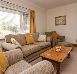 A living room with beige sofas yellow curtains a wooden coffee table and a framed map on the wall at Lyndhurst in Ambleside