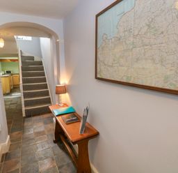 A hallway with tiled floor a wooden bench with a lamp folders and a map on the wall at Orielton Cottage in Dinas Cross