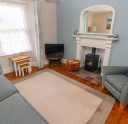 A living room with a grey sofa and armchair a fireplace with a stove and a TV on a small table at Orielton Cottage in Dinas Cross