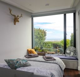 A bedroom with a bed near a large window with plants and a fan at Sunriser in Tara Hill near Ballymoney County Wexford