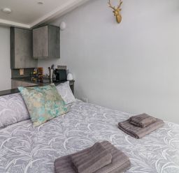 A bedroom with a bed with patterned bedding and folded towels next to a small kitchen area with cabinets and a coffee machine at Sunriser Tara Hill near Ballymoney County Wexford