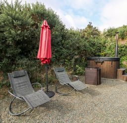 Two lounge chairs with a closed red umbrella and a wooden hot tub in a garden at Sunriser Tara Hill near Ballymoney County Wexford