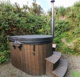 An outdoor wooden hot tub with a cover and steps surrounded by bushes at Sunriser in Tara Hill near Ballymoney County Wexford