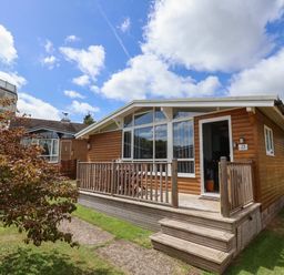 A wooden cabin with a deck and steps in a grassy yard at Pebble Beach Chalet in Seaton