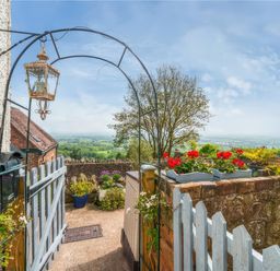 A garden entrance with a blue gate flowers in pots and a countryside view at Holly Cottage in Great Malvern