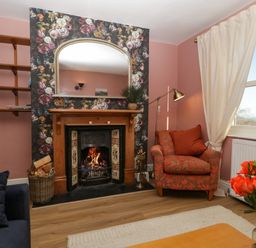 A living room with a fireplace an armchair a window and a bouquet of orange roses at Holly Cottage in Great Malvern