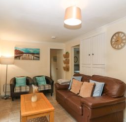 A living room with a brown leather sofa pillows two black armchairs wooden coffee table and wall clock at 245 Riverside Lodge in Caeathro