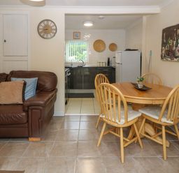 A dining area with wooden table and chairs next to a kitchen and a brown leather sofa with cushions at 245 Riverside Lodge in Caeathro
