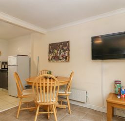 A dining area with wooden table and chairs next to a wall-mounted TV and a small side table with board games at 245 Riverside Lodge in Caeathro